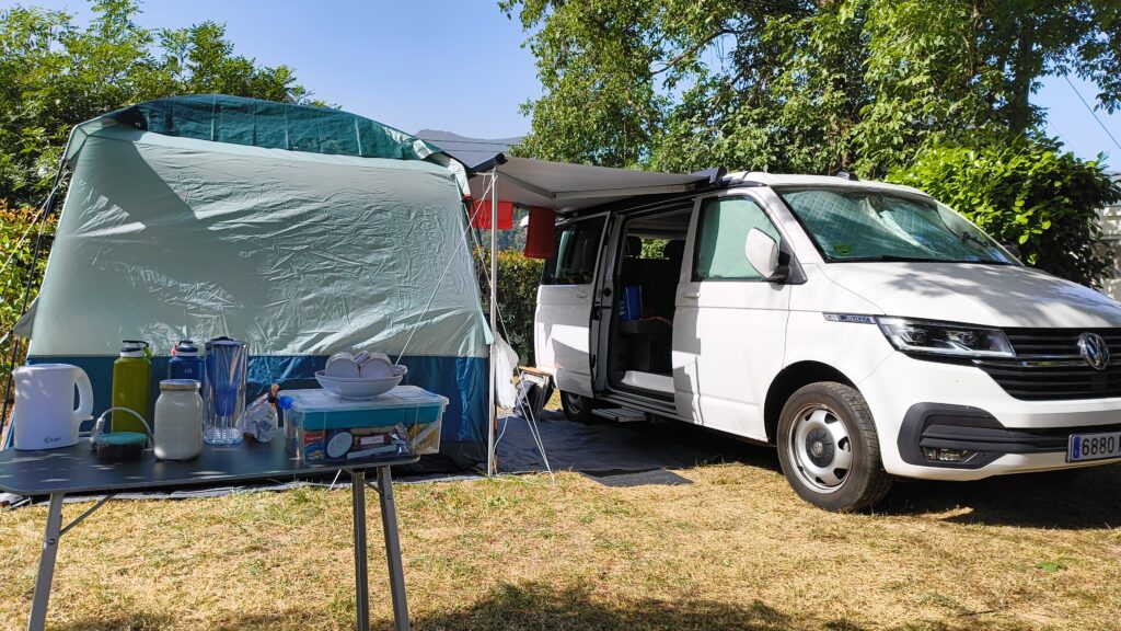 A VW campervan with its awning out. Attached is a tent.