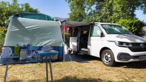 A VW campervan with its awning out. Attached is a tent.